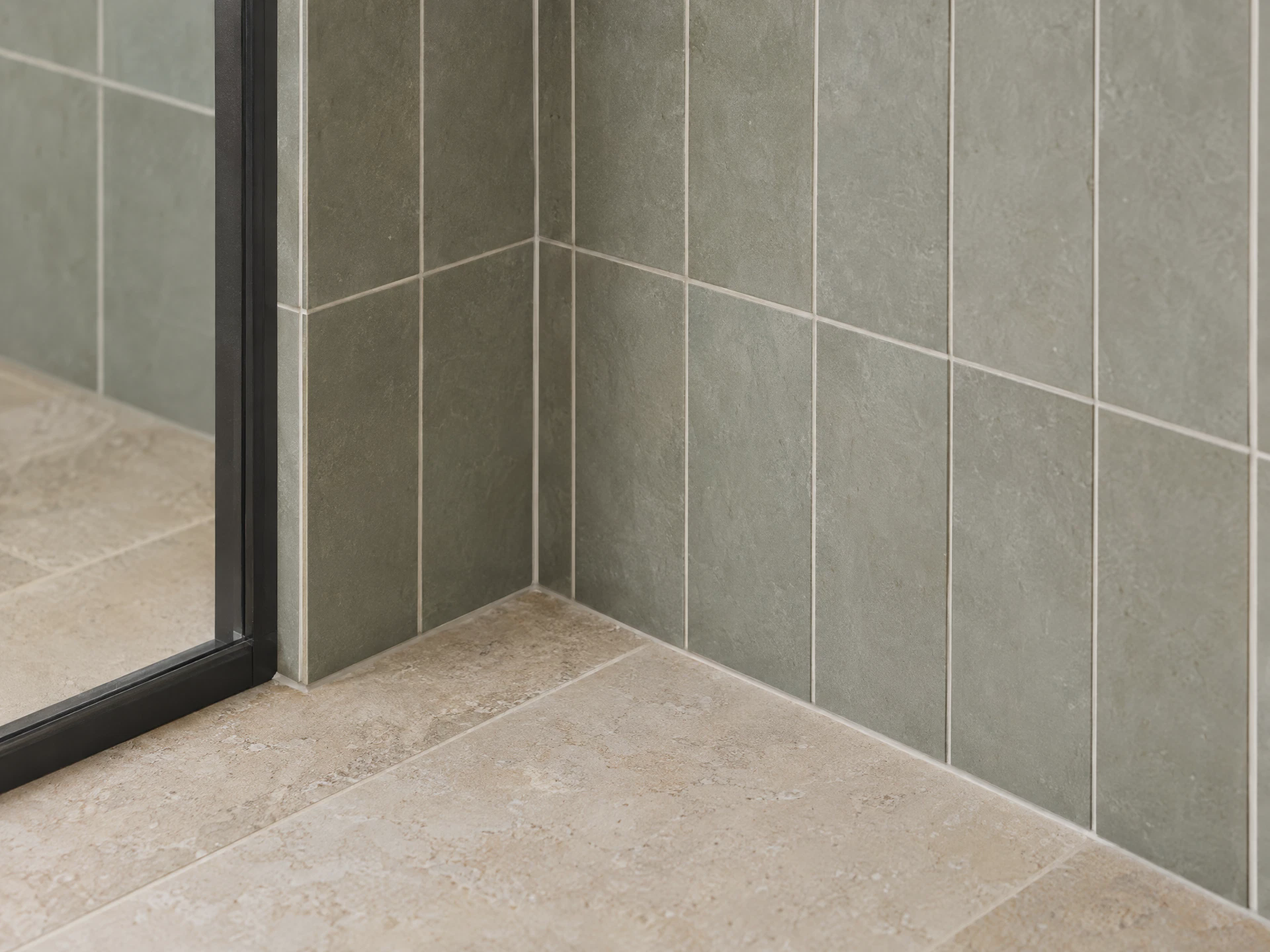 Sage-gray bathroom wall tile meeting a limestone floor