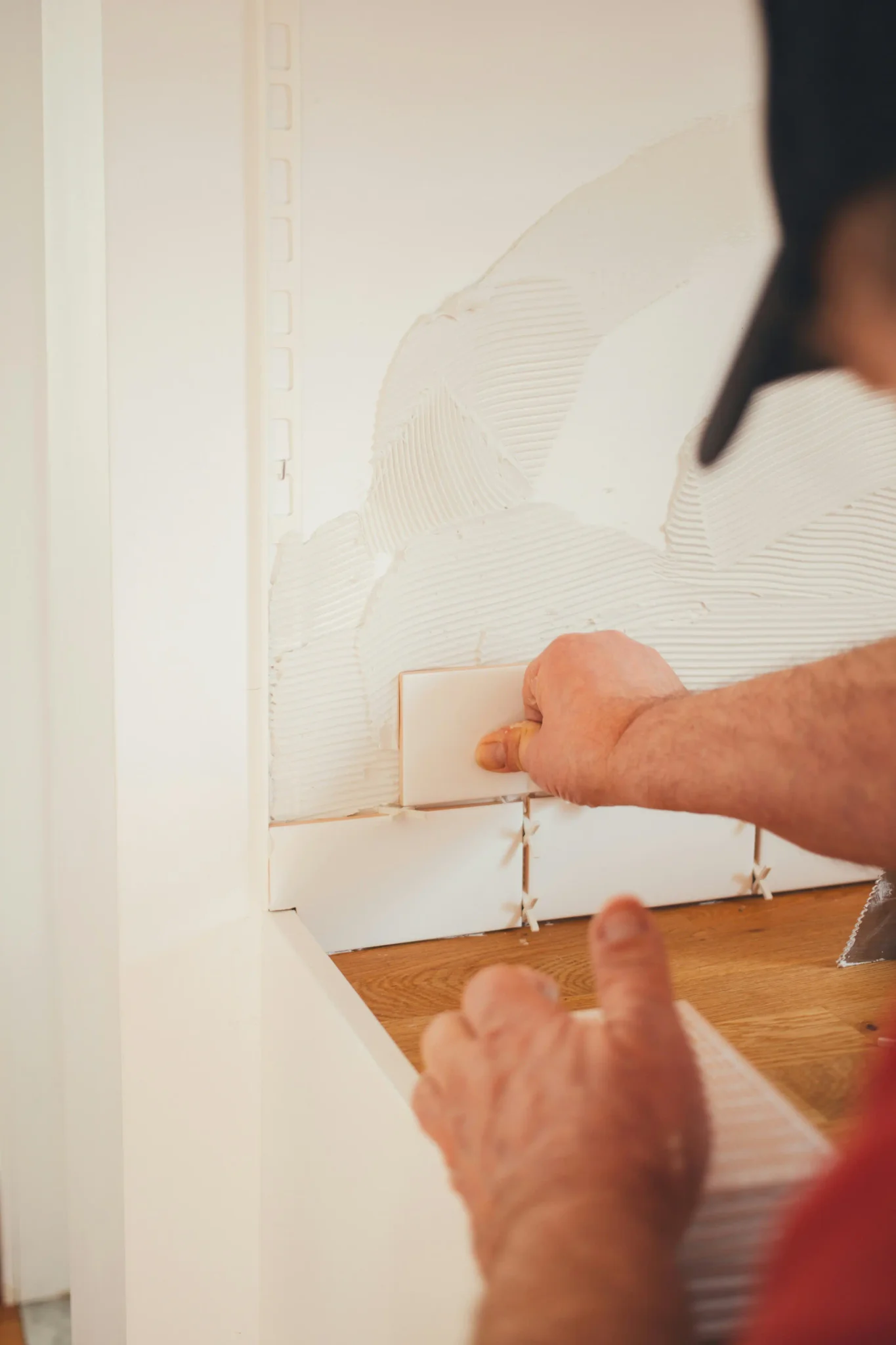 Tile installer pressing small white square tiles onto adhesive-covered wall during installation